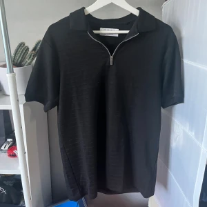 Svart pikétröja med dragkedja  - Svart pikétröja från Primark i regular fit med korta ärmar och krage. Tröjan har en snygg dragkedja framtill istället för klassiska knappar. Perfekt för en clean och stilren look, passar till jeans eller shorts. Är XS men passar till och med M. Inga defekter. 