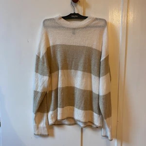 Tjock tröja/ Koszula - Säljer en stickad tröja från H&M Divided i storlek S. Tröjan har breda beige och vita ränder, rund hals och ribbade muddar vid ärmslut och nederkant. 