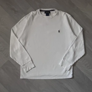  Polo Ralph Lauren Thermal Vit Strlk M - Vit långärmad tröja från Polo Ralph Lauren i bomull med diskret broderad logga på bröstet. Tröjan har en klassisk rund halsringning och är tillverkad i ett strukturerat tyg som ger en snygg och stilren look.