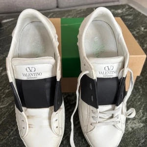 Valentino Garavani vita sneakers strl 38.5 - Low-top buffed recycled faux-leather sneakers in white.  · Signature pyramid studs throughout · Logo patch at padded tongue · Padded collar · Text printed at outer side · Textured rubber midsole · Treaded rubber sole  Supplier color: Black/Bianco  Including: Original box Original shoelaces x 2 Original Dust bag