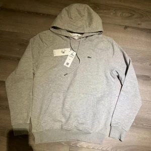 Grå Lacoste Hoodie  - Tjena säljer denna nya Lacoste hoodien i storleken S grå färg. Står L men den är väldigt liten i storleken och passar S. Riktigt fin, skriv gärna vid intresse! 