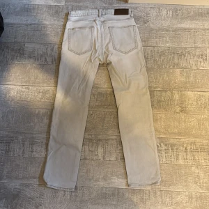 Ljusgrå jeans från Dressmann - Snygga ljusgrå jeans från Dressmann med klassisk femficksdesign och raka ben. Jeansen har silverfärgade nitar och knapp, samt en mörkbrun läderpatch bak i midjan. Perfekt för dig som gillar stilrena och neutrala färger.