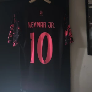 Nike Brasil Neymar Jr. Dri-Fit tröja S - Säljer en svart och neonrosa Brasilien fotbollströja från Nike med Neymar Jr. och nummer 10 på ryggen. Tröjan har korta ärmar och ett unikt grafiskt mönster med Kristusstatyn och andra detaljer. Tillverkad i Dri-Fit material som andas.