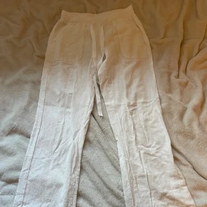 Vita linnebyxor med snörning - Säljer ett par tunna vita linnebyxor med bred resår i midjan och snörning framtill. Byxorna har raka ben och två stora fickor framtill. Perfekta för varma dagar och chill vibes.