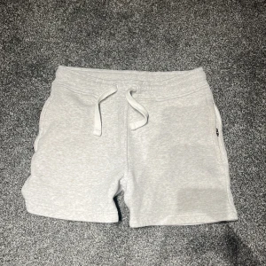 Fräsha Russemerch kortbyxor - Säljer ett par ljusgrå mjukisshorts från Russemerch i storlek S. De har elastisk midja med snörning, sidofickor och en bakficka. Perfekta för chill dagar eller när du vill vara bekväm. Materialet är mjukt och känns skönt mot huden. Knappt använda. Köpta för 400