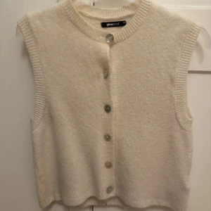 Beige stickad väst från Gina Tricot - Supermysig beige stickad väst från Gina Tricot med rund halsringning och stora knappar framtill. 