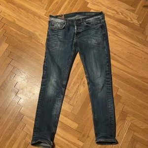 Blå jeans från Dondup  - Säljer ett par blå jeans från Dondup med snygga slitningar men också lite defekter på insadan av lilla fickan och på insidan av jeansen med detaljerade sömmar. Jeansen har klassisk femficksdesign och knappstängning samt coola kontrastsömmar. Passformen är smal och benen är raka med lätt tvättad look.