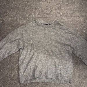 Grå stickad tröja från 157 - Mysig grå stickad tröja från 157 med rund halsringning och ribbade muddar vid ärmslut och nederkant. Perfekt för lager-på-lager och chill dagar. Enkel och stilren design som funkar till det mesta.