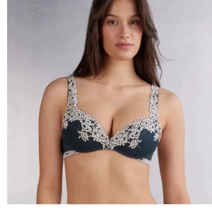 Mörkblå spets-bh med blommig kant - Superfin mörkblå bh med ljus spets i blommigt mönster längs kanterna och axelbanden. Bh:n har vadderade kupor och ger en snygg form. Perfekt för dig som gillar detaljer och vill ha något extra under kläderna.