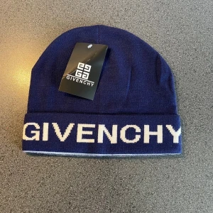 Mörkblå mössa från Givenchy - Snygg mörkblå mössa från Givenchy med vit logotyp framtill. Mössan är ribbstickad och har en uppvikt kant. Insidan är vit med en Givenchy-etikett. Perfekt accessoar för att lyfta din stil under kyliga dagar.