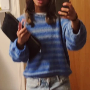 Blå randig stickad tröja - Säljer en mysig blå stickad tröja med ljusblå och vita ränder. Tröjan har en avslappnad passform och långa ärmar, perfekt för att hålla sig varm under kyliga dagar. Den har en klassisk rund hals och mjukt material som känns skönt mot huden.