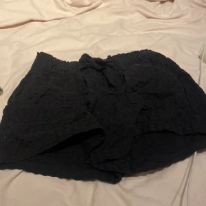 Svarta shorts med snörning - Svarta, lösa shorts med bekväm resår i midjan och snörning framtill. De har en lätt struktur i tyget och är perfekta för varma dagar. Passar dig som gillar en avslappnad och enkel stil.