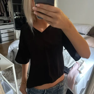 Svart blus med v-ringning från Lindex - Svart blus från Lindex i storlek XS med v-ringad hals och vida, korta ärmar. Silkes material. 