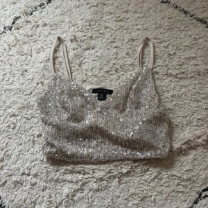 Glittrig paljettopp från Amisu XS - Supersnygg glittrig topp från Amisu i storlek XS. Toppen är täckt av silvriga paljetter och har smala axelband. Den är croppad och har en ljus beige bas. Perfekt för dig som vill sticka ut med lite extra bling.