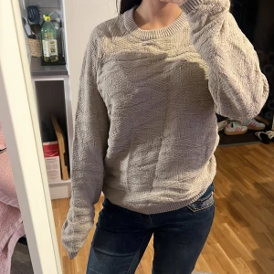 Beige stickad tröja från SMOG - Säljer en beige stickad tröja från SMOG i storlek S. Tröjan har ett snyggt strukturerat mönster och ribbade muddar vid hals, ärmslut och nederkant. Slim fit-modell som sitter snyggt på kroppen och passar perfekt till jeans.