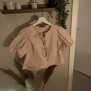 Ljusrosa blus med puffärm från Gina Tricot - Supersöt ljusrosa blus från Gina Tricot med puffiga korta ärmar och snygg snörning framtill. Blusen har en rundad hals och är tillverkad i ett mjukt bomullsmaterial. Perfekt för dig som gillar romantiska detaljer och vill sticka ut lite extra.