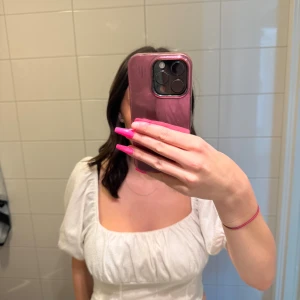 Vit croppad blus med puffärm - Säljer en vit croppad blus med fyrkantig ringning och puffiga korta ärmar. Toppen har en lätt rynkad detalj framtill och sitter snyggt i midjan. Perfekt för dig som gillar romantisk och trendig stil.