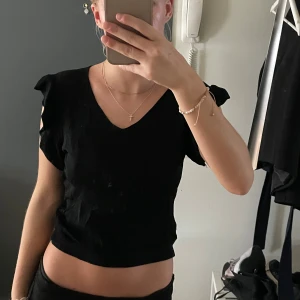 Svart topp med volangärm - Säljer denna svarta topp med volang armar och ett tunt ribbat material, den är superskönt att ha på sig och passar till allt. Tyvärr vet jag inte vart den är ifrån då den är köpt i Spanien och storlek är jag lite osäker på men det är typ xs/s