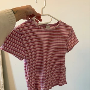 Randig ribbad topp i rosa och vit - Superfin kortärmad topp från nelly i ribbat material. Toppen har ett randigt mönster i rosa, rött och vitt och en klassisk rund halsringning. Perfekt för dig som gillar en söt och avslappnad stil.
