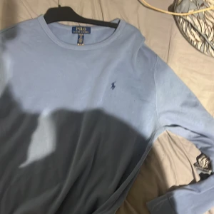 Ljusblå långärmad tröja Polo Ralph Lauren - Snygg ljusblå långärmad tröja från Polo Ralph Lauren med klassisk rund hals och den ikoniska broderade loggan på bröstet. Tröjan är tillverkad i mjuk bomull och har en clean, stilren look som funkar till jeans eller chinos.