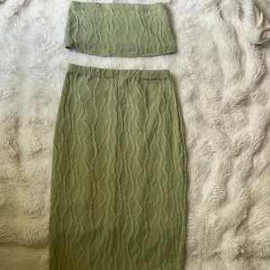 Olivgrön långkjol med strukturmönster och matchande topp  - Säljer en olivgrön långkjol med snyggt strukturmönster i vågiga linjer. Kjolen har en rak passform och resår i midjan för extra komfort. Materialet känns mjukt och stretchigt, perfekt för en trendig och avslappnad look. ( TOPP INGGÅR)