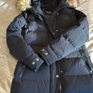 Svart pufferjacka från Hollies  - Svart pufferjacka från Hollies. Jackan har dragkedja, knappar och flera fickor med dragkedja. Klassisk logga på ärmen och fina detaljer vid ärmslut. Bara använd en vinter! Perfekt för vintern.