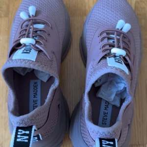 Chunky sneakers från Steve Madden - Säljer ett par chunky sneakers från Steve Madden i en snygg lila-beige ton. Skorna har stickad ovandel i syntetmaterial, elastisk snörning med vita detaljer och bred, mönstrad sula. Bak finns en svartvit flik med text. Perfekta för dig som gillar streetstyle.