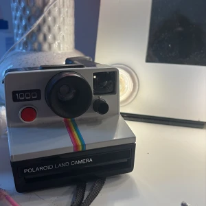 Polaroid Land Camera 1000 - Säljer en Polaroid Land Camera 1000 med den klassiska regnbågsranden 🌈 En riktigt retro ikon som inte dyker upp så ofta. Kameran är i bra skick och funkar som den ska – perfekt för dig som vill få den där äkta polaroidkänslan direkt i handen 📸 Perfekt både för användning och som samlarobjekt