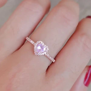 Hjärtformad ring med rosa sten - Superfin ring med hjärtformad ljusrosa sten i mitten, omgiven av små glittrande stenar. Ringen har en tunn, glittrig band och ger en romantisk och söt vibe. Perfekt för dig som älskar detaljer och vill sticka ut. Liknande ring finns av märket pandora