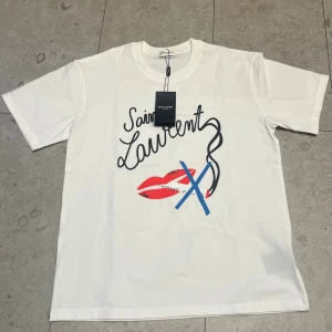 Saint Laurent t-shirt - Snygg och trendig no smoking t shirt från saint laurent med ett ikoniskt tryck. Gjord i mjuk bomull av högsta kvalitet, med en avslappnad men stilren passform. En tidlös statement-piece som är både cool och enkel att styla – funkar lika bra till jeans och sneakers som under en kavaj för en mer edgy look.