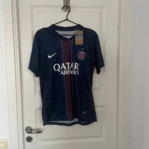 PSG matchtröja Nike M - Snygg PSG fotbollströja från Nike i marinblått med röd och vit detalj på framsidan. Tröjan har klubbmärke, Qatar Airways-tryck och korta ärmar. Tillverkad i lätt och ventilerande material, perfekt för match eller träning.