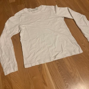 Vit långärmad tröja från Weekday - En basic vit långärmad tröja från Weekday i mjuk bomull. Enkel och clean design med rund halsringning och normal passform. Perfekt att styla lager på lager eller bära som den är. Storlek S.