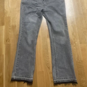 Grå Zara flare Jeans  - Säljer ett par grå jeans med rak passform och rå, fransad kant längst ner. Jeansen har klassisk femficksdesign och är tillverkade i denim. Perfekta för dig som gillar en avslappnad och trendig stil.