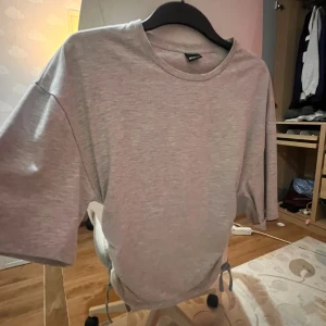Ljusgrå t-shirt med snörning - Säljer en ljusgrå t-shirt från Gina Tricot med korta ärmar och rund hals. Det är tajt rund midjan och väldigt bekväm. Nästan aldrig använt!🩷