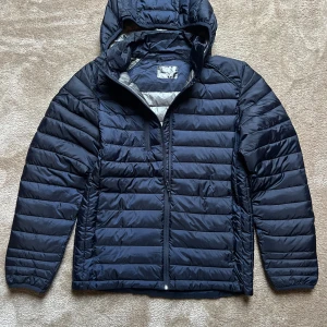 Mörkblå pufferjacka  - Säljer den här vinterjackan med en huva som går att ta av för att den inte passade mig. Den har aldrig används och är i nyskick. Den är perfekt för vinter och nypriset är 1000 kr.