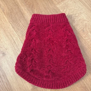 Röd stickad tröja från Little Bigger (hund) - Säljer en röd stickad tröja från Little Bigger i storlek S. Tröjan har ett snyggt flätmönster och ribbade kanter. Perfekt för att hålla värmen under kyliga dagar. Passar dig som gillar klassisk och mysig stil.