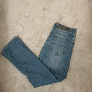 Blå jeans TOS 29/32 - Snygga blå jeans från tiger of Sweden i slimfit. Klassisk femficksdesign. Perfekta till vardags med en enkel t-shirt eller hoodie. Jeansen har en ljus tvätt och är tillverkade i mjukt denimtyg.