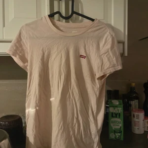 Ljusrosa t-shirt från Levi's - En stilren ljusrosa t-shirt från Levi's med klassisk rund hals och liten röd logotyp på bröstet. Modellen är kortärmad och i mjuk bomull, perfekt till jeans eller shorts. Snygg basic som funkar året runt.