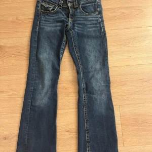 Blå bootcut jeans low waist  Gina Tricot 152 - Snygga blå jeans från Gina Tricot i storlek 152. Modellen har bootcut-ben, klassiska fickor och dubbla silverknappar framtill. Jeansen har kontrastsömmar och en cool tvättad look. Perfekta för dig som gillar en avslappnad men trendig stil.