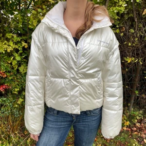 Vit pufferjacka från Calvin Klein Jeans - Snygg vit pufferjacka från Calvin Klein Jeans med avtagbara ärmar så den kan bäras som väst. Jackan har hög krage, dragkedja och tryckknappar framtill samt diskret logga på bröstet. Perfekt för vintern, snygg och trendig!