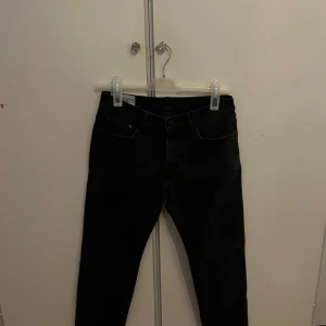 Svarta jeans med fem fickor - Svarta jeans med klassisk femficksdesign och smal passform. Jeansen har knapp och dragkedja framtill samt bakfickor. Materialet är jeans och färgen är mörk svart, vilket ger en stilren look. Perfekta för dig som gillar en tight siluett.