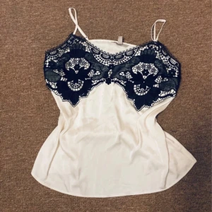 Vit och svart linnetopp från H&M - Supersnygg vit linnetopp från H&M med tunna axelband och svart spetsdetalj. Säljer vidare eftersom den inte kom till användning