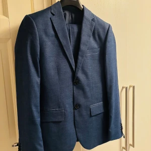 Kostym - Snygg blå kostym från H&M i slim fit-modell. Kavajen har två knappar. Byxorna har en stilren look och matchar kavajen perfekt. Materialet är en blandning av polyester, viskos och bomull för en bekväm känsla. Storlek 44 och passar S/M. Köpt för 1499kr. Skriv för funderingar!