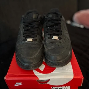 Nike Air Force 1 helsvarta sneakers - Säljer ett par klassiska helsvarta Nike Air Force 1 sneakers i skinn. Modellen har låg profil, rund tå, perforerad tåbox och svart sula. Snygga och tidlösa med svart snörning och diskret Nike-logga på sidan och hälen.