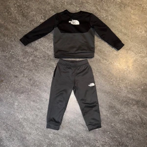 Dress från The North Face - Svart dress från The North Face med vit logga på vänster lår. Settet har elastisk midja och muddar vid bensluten för en skön passform. Perfekta för chill eller träning, tillverkade i mjukt syntetmaterial. 3T, 92/98