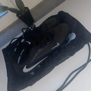 Nike Phantom fotbollsskor svart/blå - Säljer ett par Nike Phantom fotbollsskor i svart med blå detaljer och vita Nike-loggor. Skorna har snörning och ribbad ovandel i syntetmaterial för extra grepp. Sulan har fasta dobbar och är designad för spel på gräs. Medföljer en svart Nike-påse. Har använt skorna 3 gånger så sjukt bra skick för sjukt bra pris 🔥