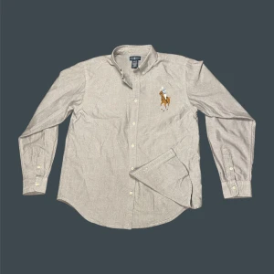 Grå skjorta från Ralph Lauren  - Snygg grå skjorta från Ralph Lauren i bomull, med klassisk button-down krage och broderad stor polospelare på bröstet. Skjortan har lång ärm, vita knappar och en stilren, normal passform. Står XL men passar S-M