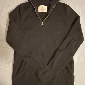 Svart ribbad half zip från Jack & Jones - Svart ribbad tröja från Jack & Jones med half zip-dragkedja och hög krage. Långärmad modell i mjuk bomull, perfekt för lager-på-lager. Enkel och stilren design som funkar till det mesta.