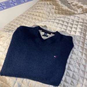 Mörkblå kashmirtröja Tommy Hilfiger - Snygg mörkblå tröja från Tommy Hilfiger i 100% kashmir. V-ringad modell med lång ärm och diskret logga broderad på bröstet. Ribbad kant vid ärmslut och nederkant ger en clean look. Perfekt för dig som gillar stilrena och mjuka plagg.