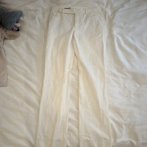 Vita kostymbyxor från Filippa K - Snygga vita kostymbyxor från Filippa K i 100% bomull. Byxorna har raka ben/ lite utsvängda, bälteshällor och två bakfickor med minimalistisk design. Perfekt för dig som gillar stilrena och klassiska plagg med modern touch.